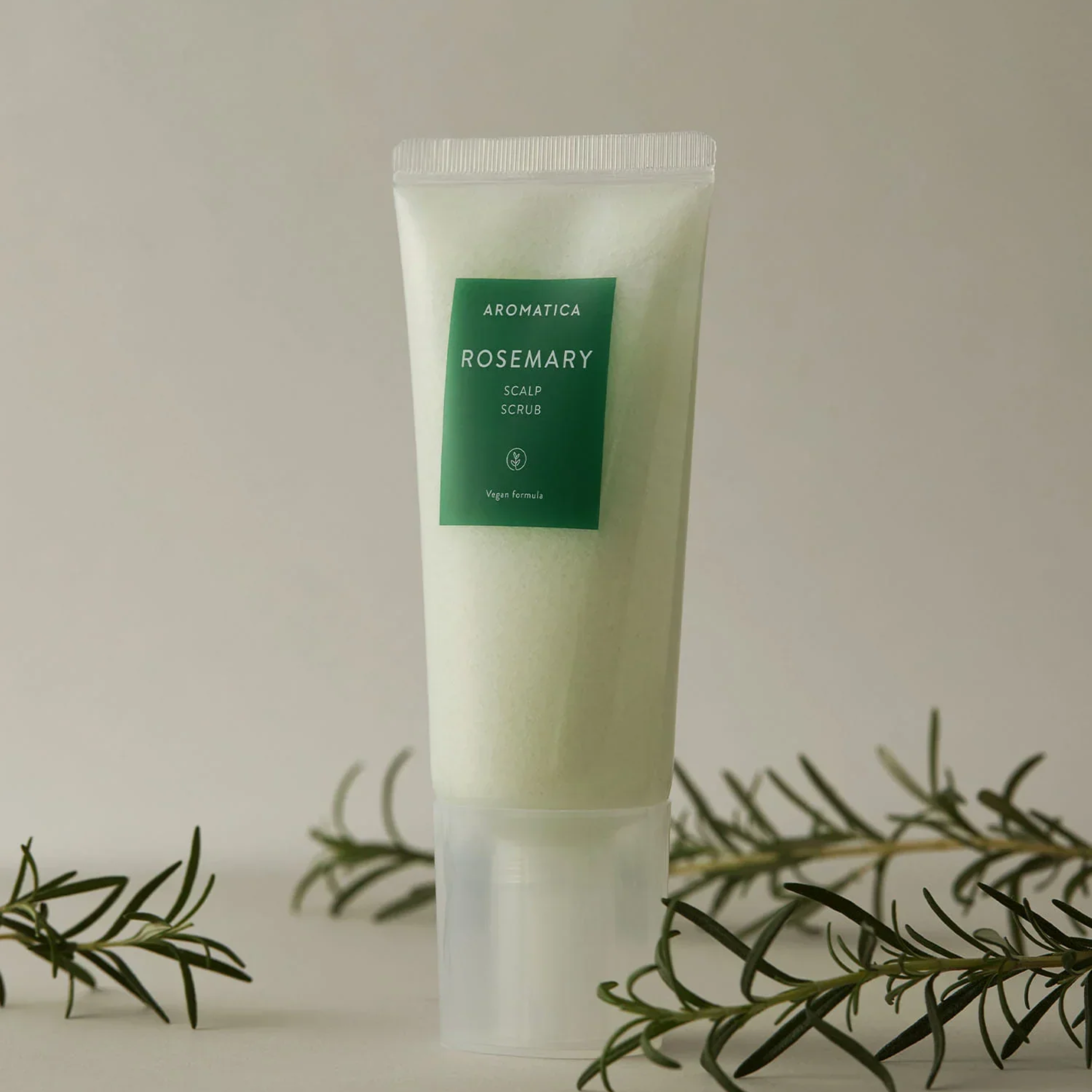 Tube of Aromatica Rosemary Scalp Scrub with rosemary leaves on a neutral background