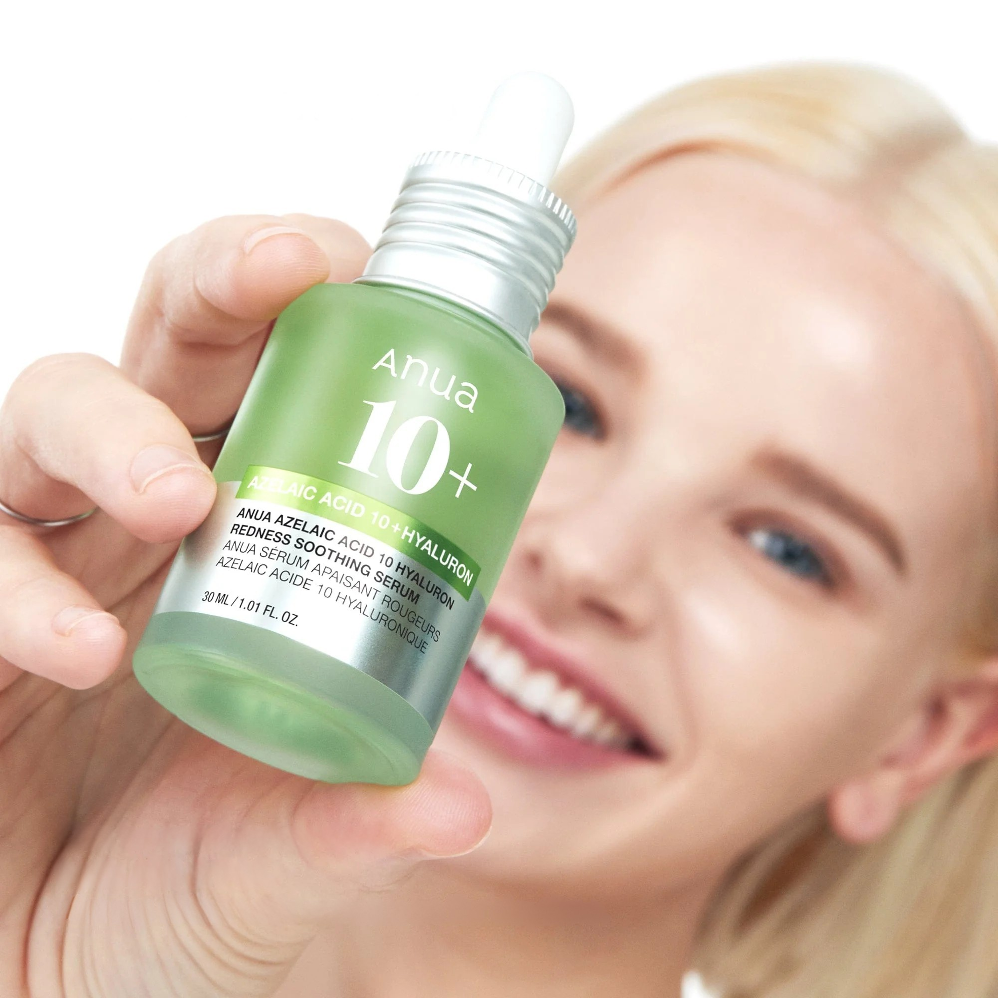 Person holding a green skincare bottle labeled 'Anua 10+' with a blurred background