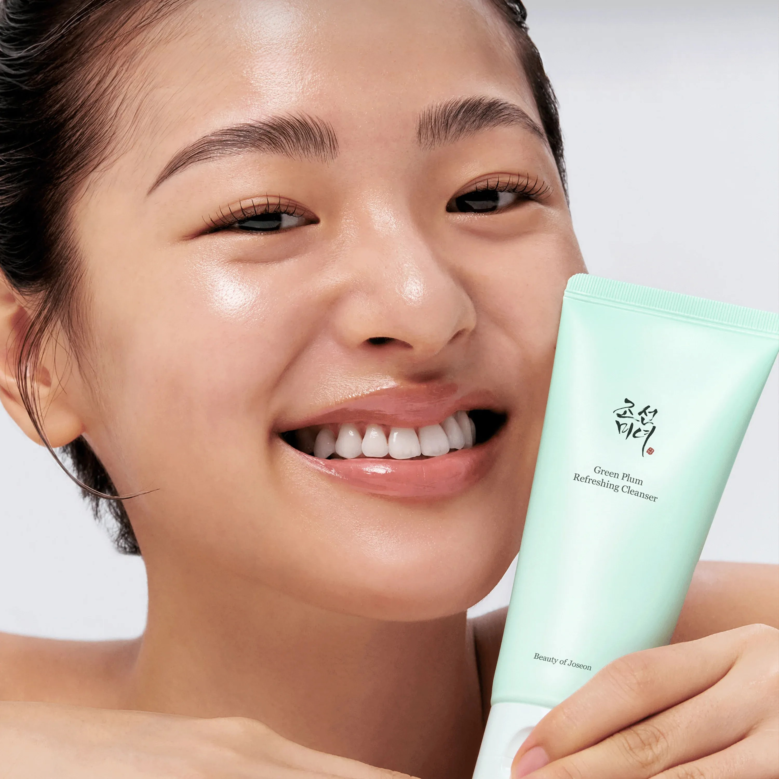 Woman holding a green skincare product with a plain background