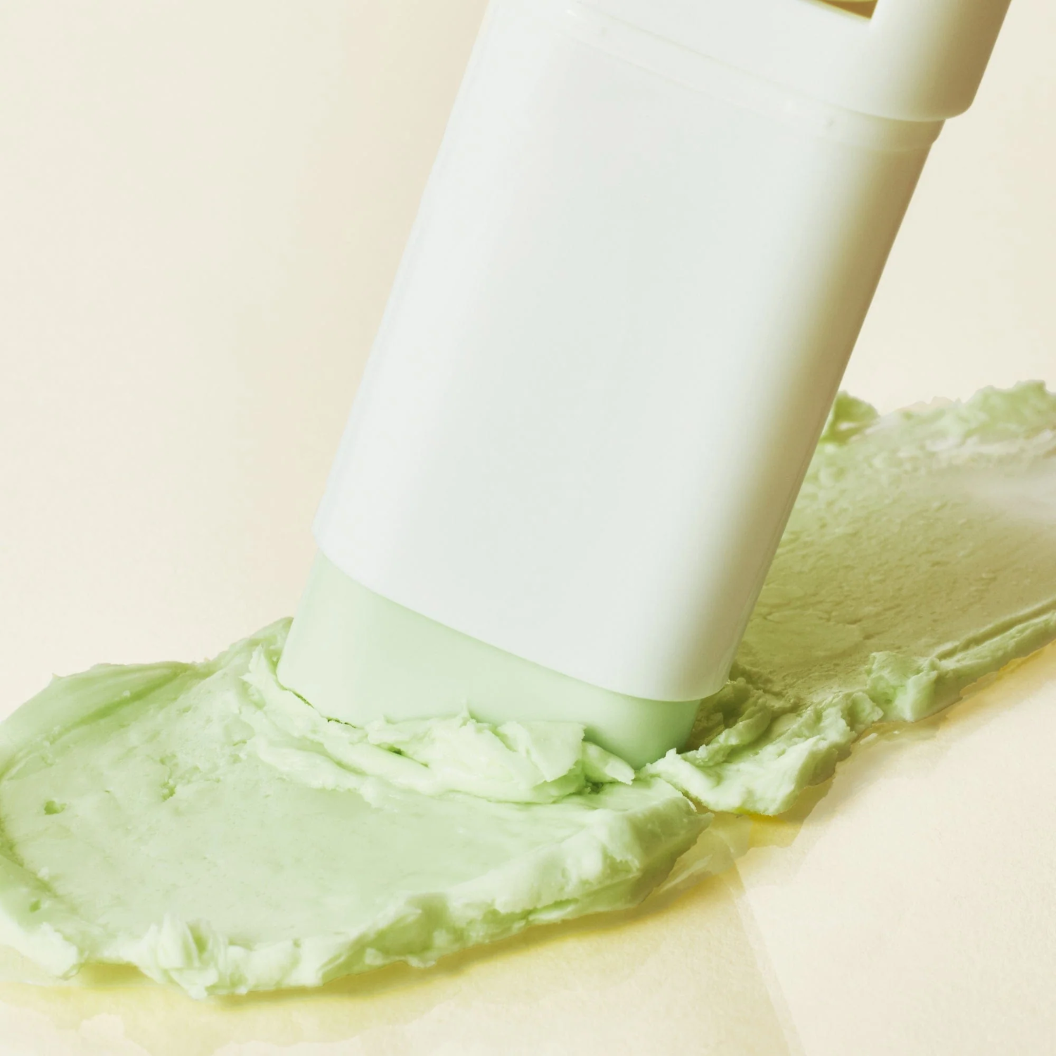 White sun stick spreading green cream on a beige background