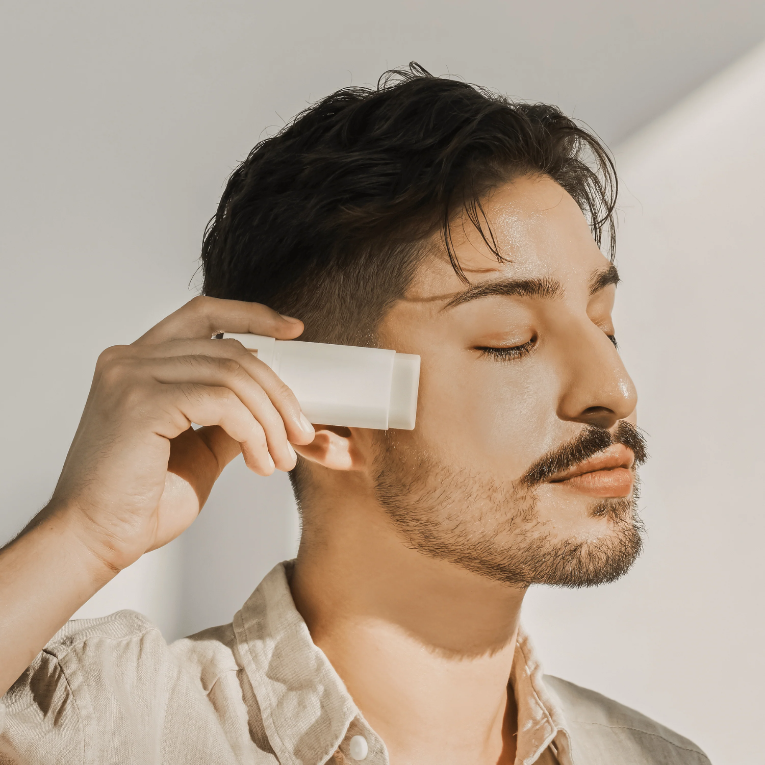 Man applying sun stick to his face with a neutral background
