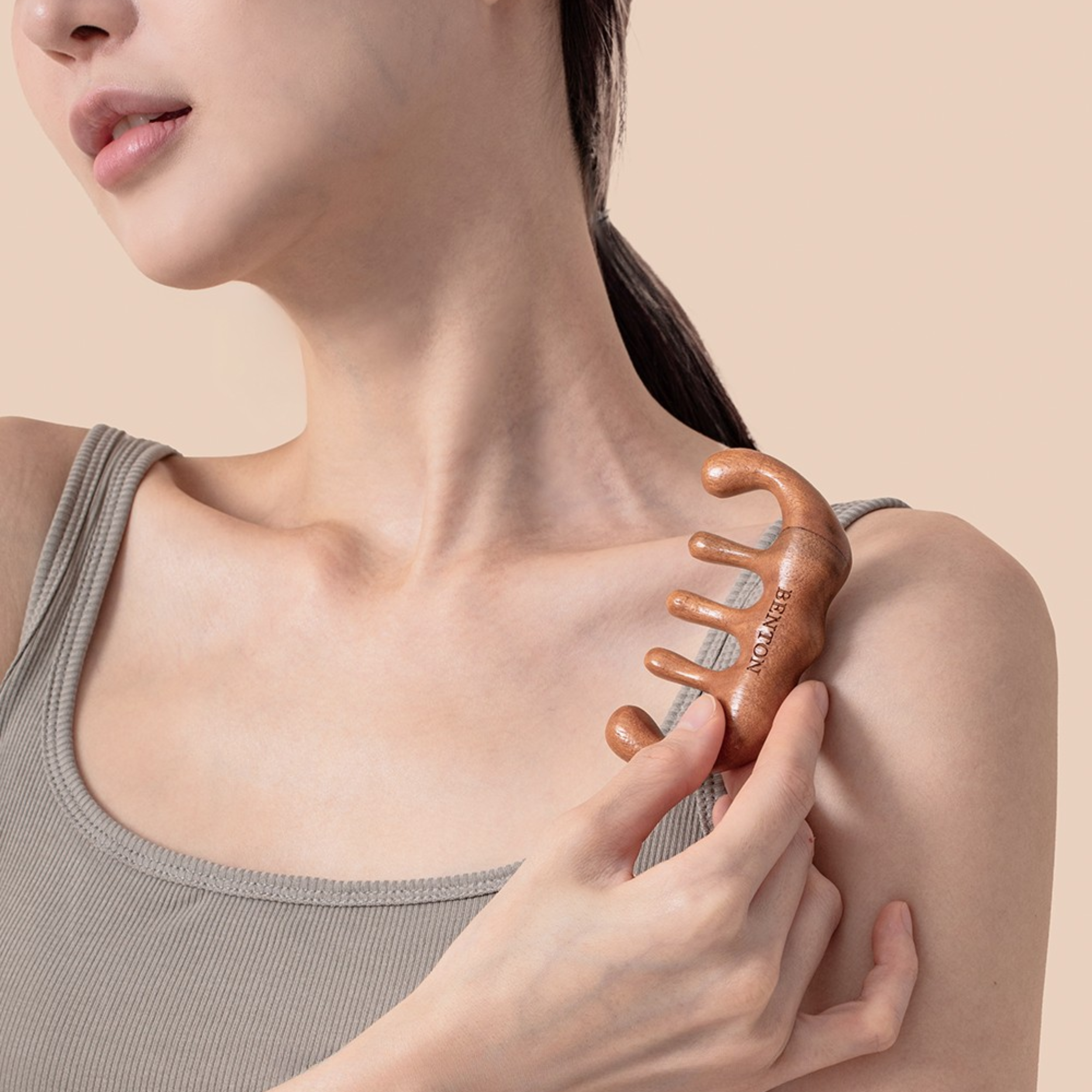 Woman using a wooden comb on her shoulder against a beige background