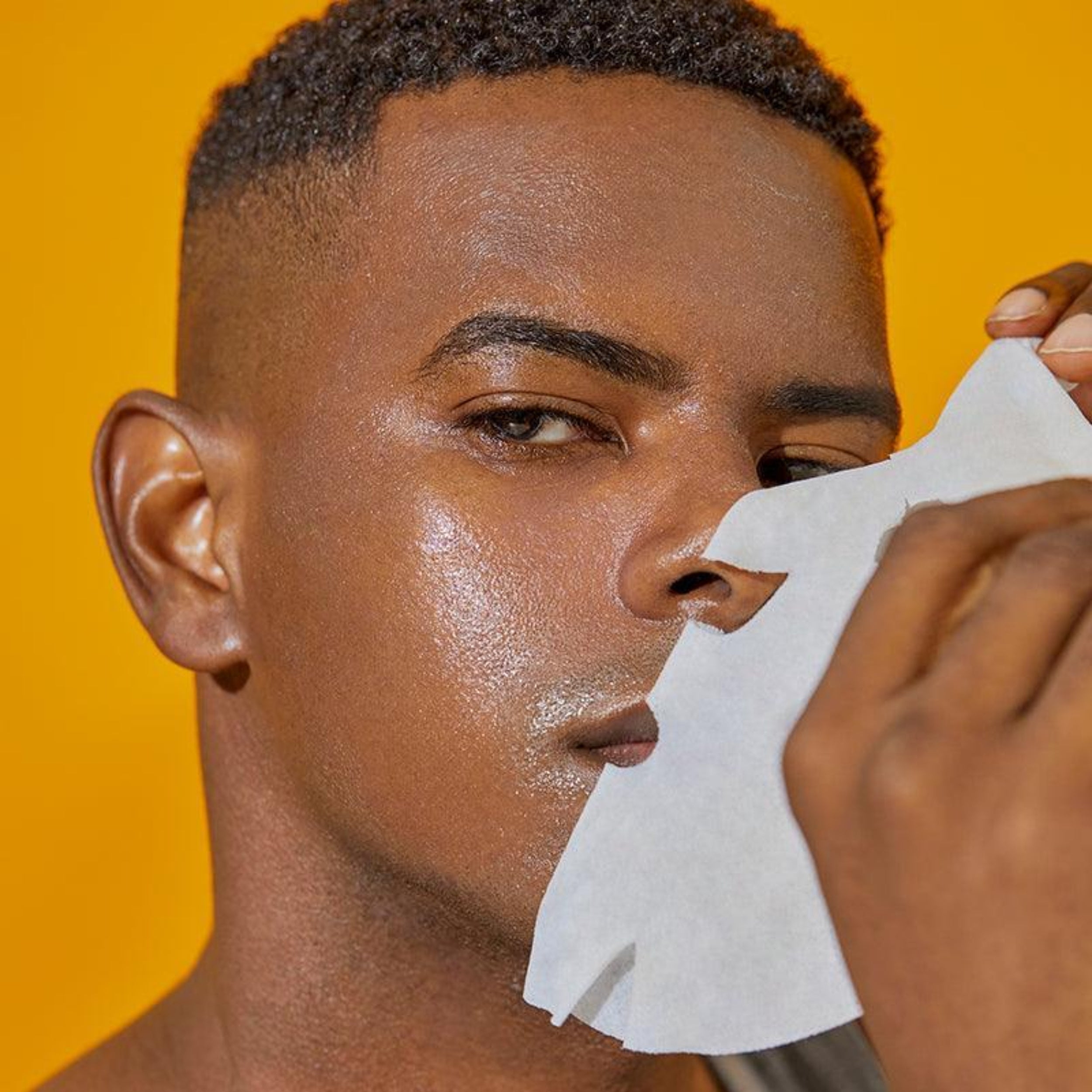 Man applying a skincare product with a white paper strip on a yellow background