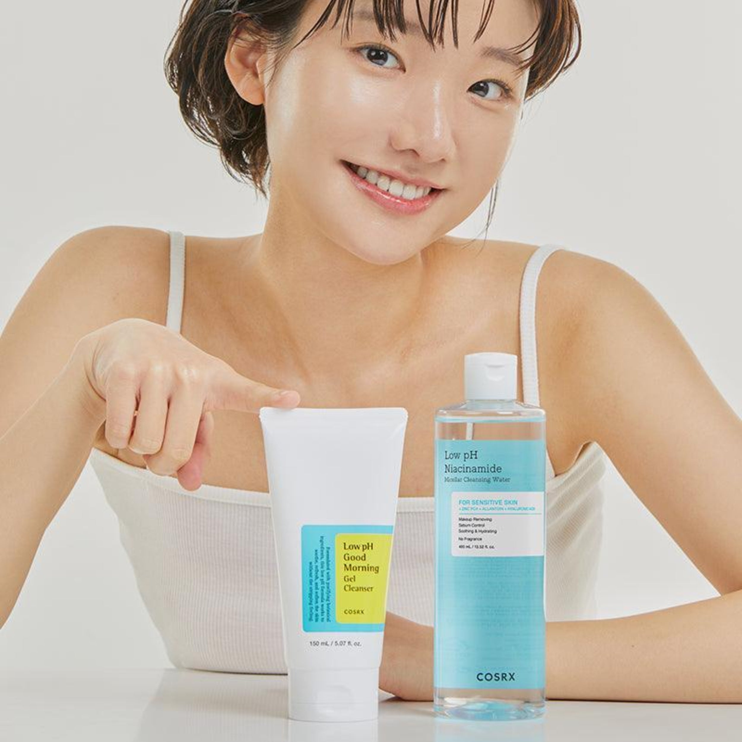 Woman holding a bottle and tube of COSRX skincare products on a white background