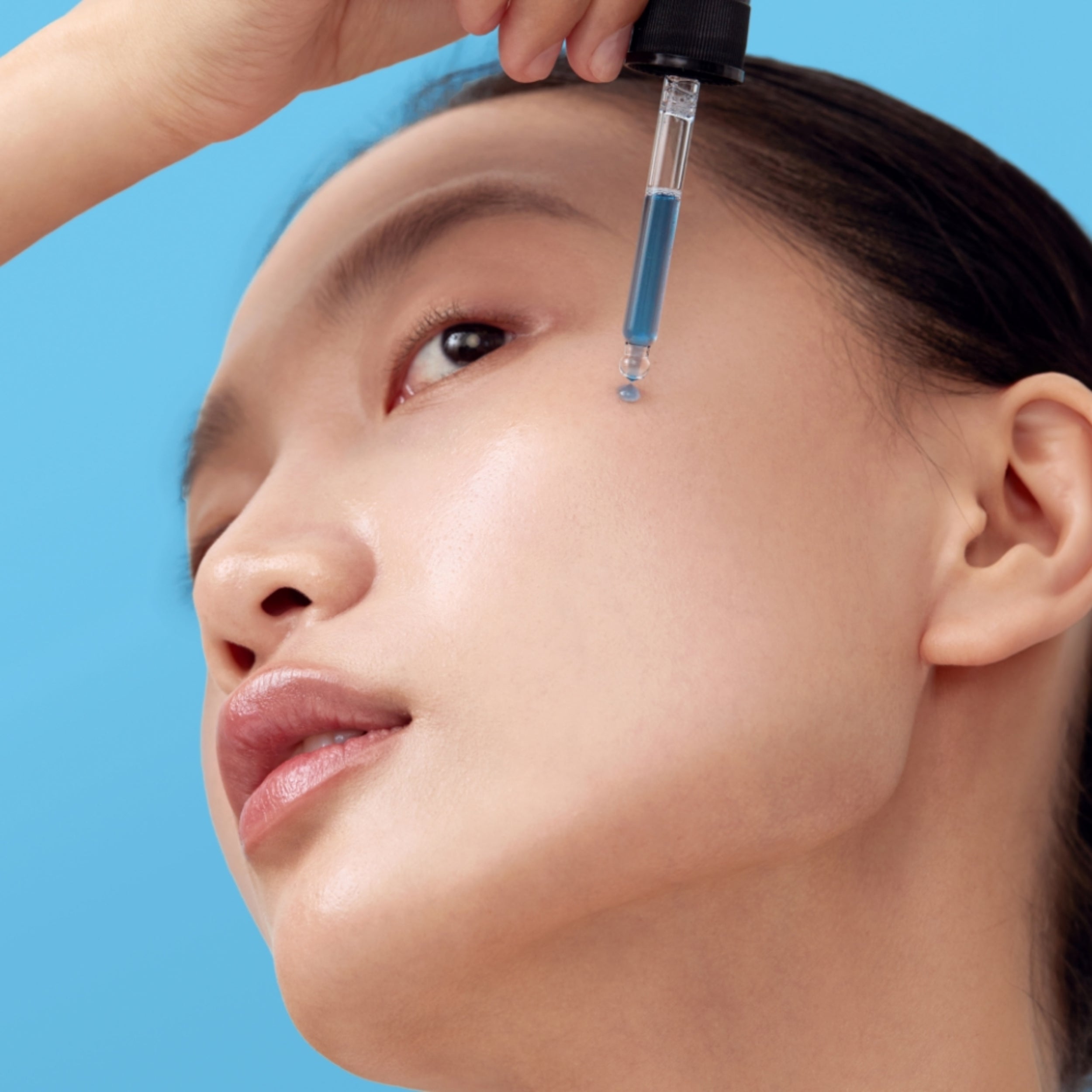 Close-up of a person applying a blue cosmetic product to their face against a blue background