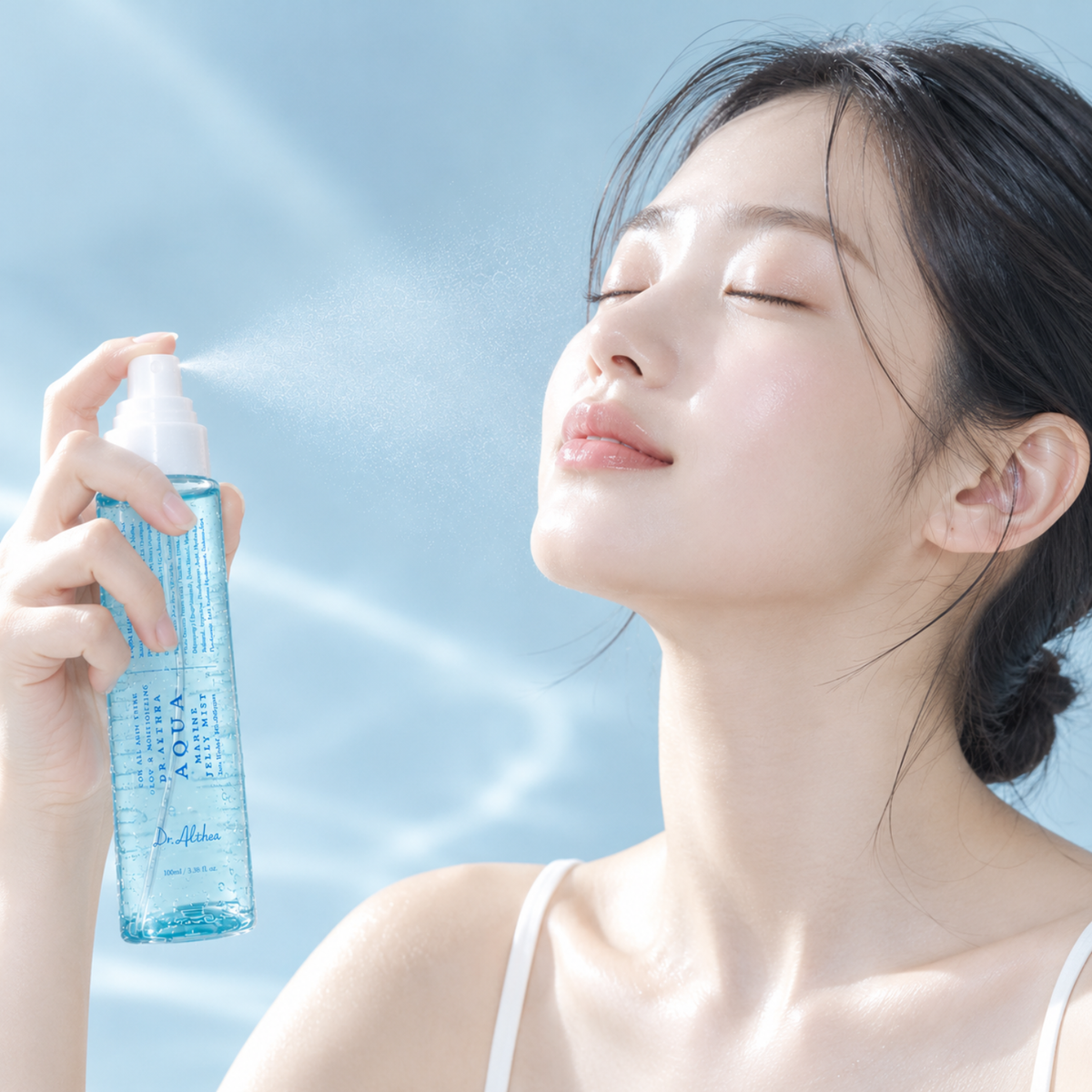 A woman with her eyes closed holds a clear spray bottle with blue liquid and white text that reads 'VIVY' and 'MIST'. She is spraying a fine mist into the air against a soft, light blue background.