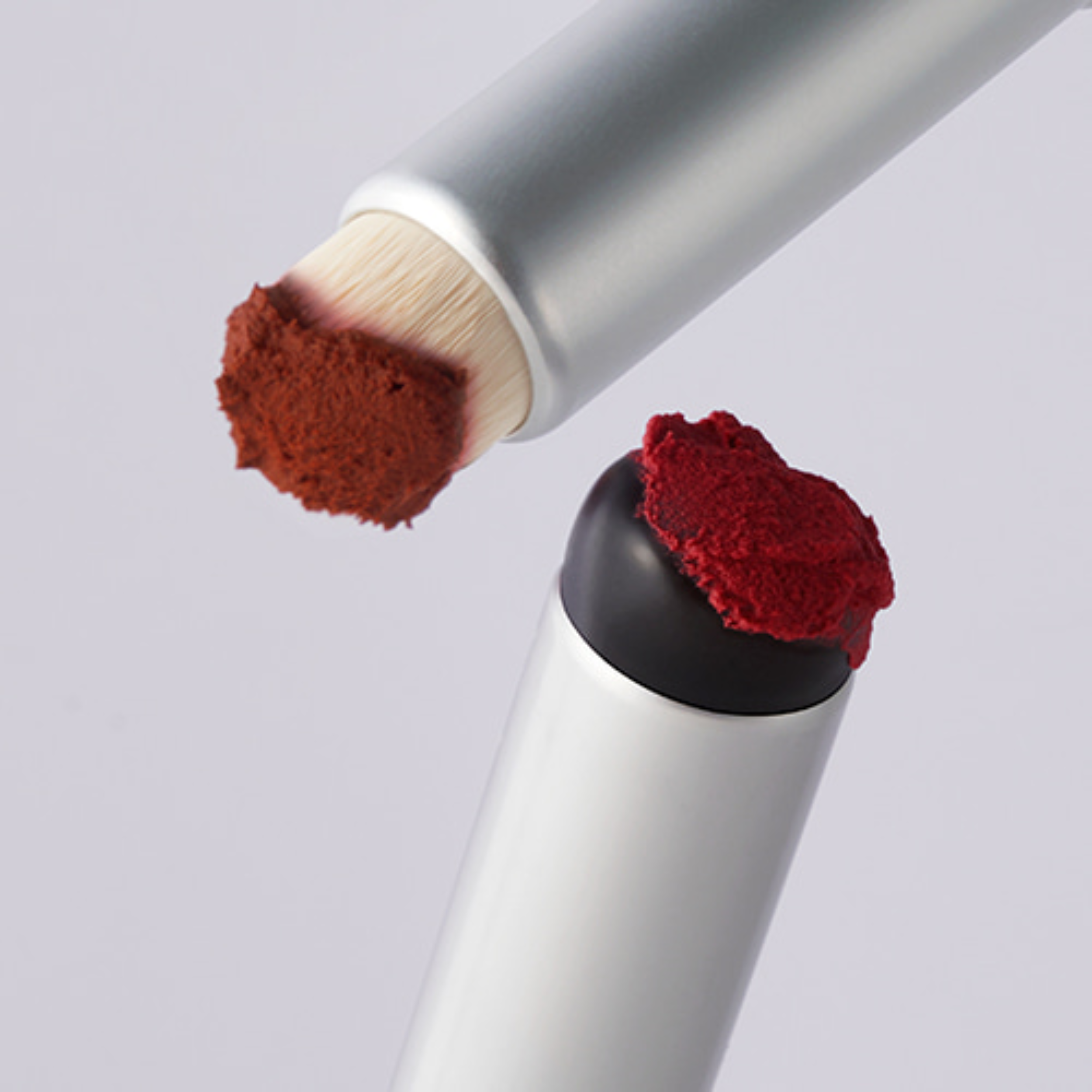 Two makeup brushes with red bristles on a light gray background