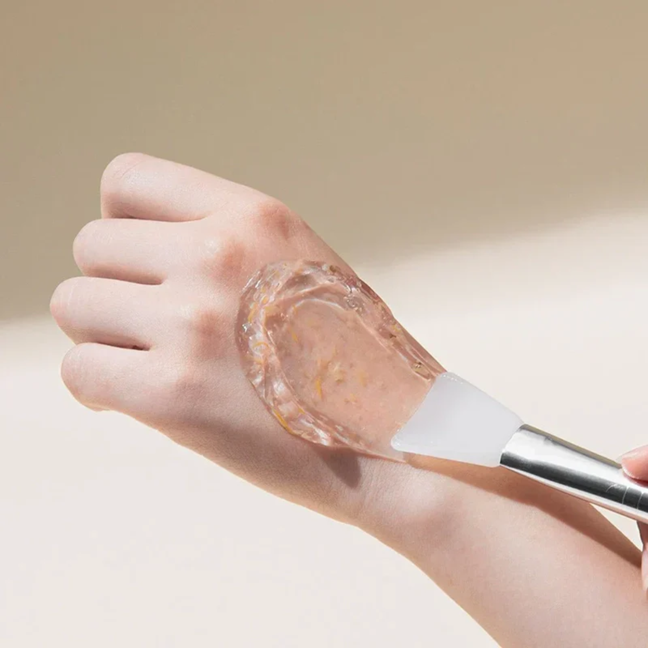 Hand applying a clear gel-like substance to another hand using a brush on a neutral background