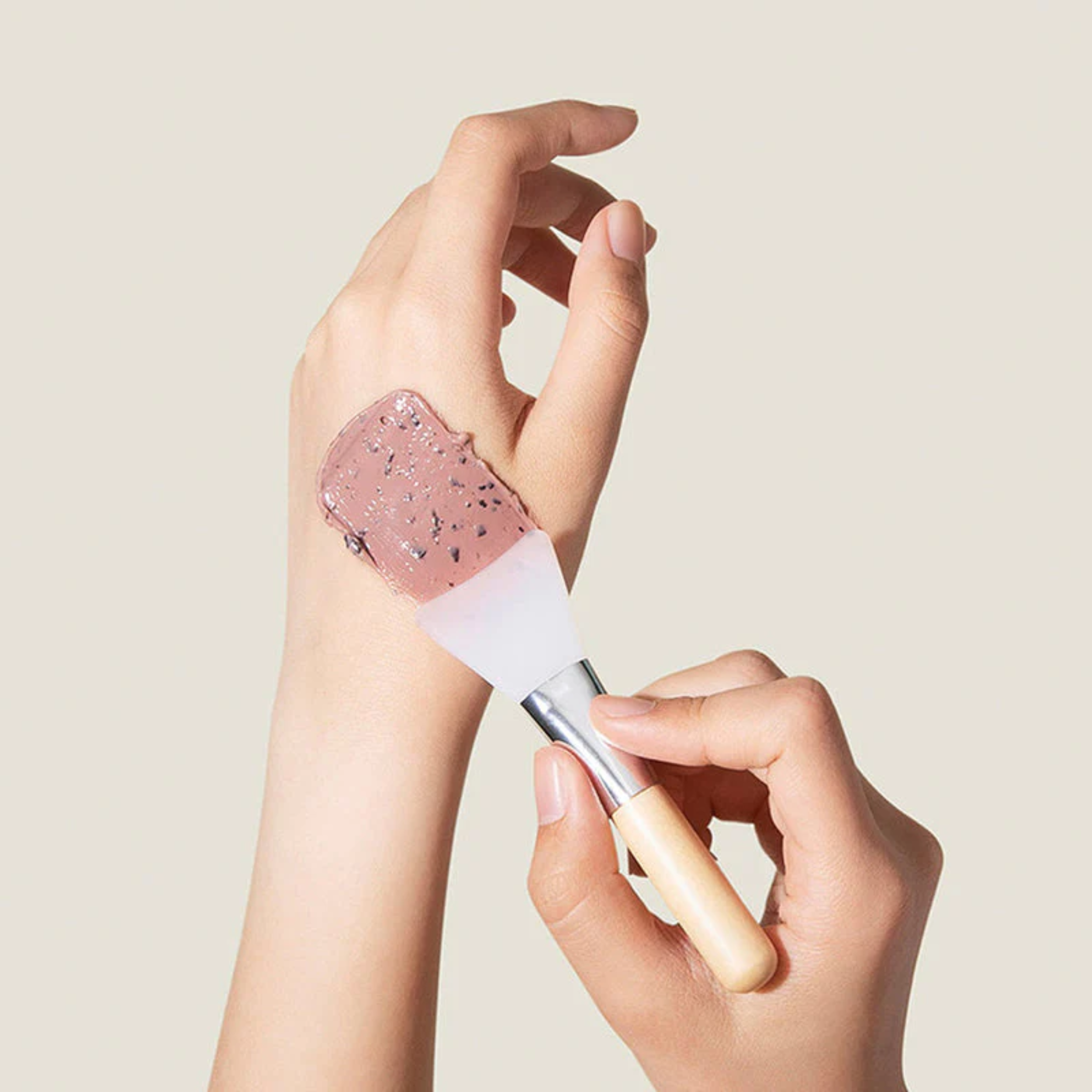Hand applying pink glittery lip balm to another hand against a beige background