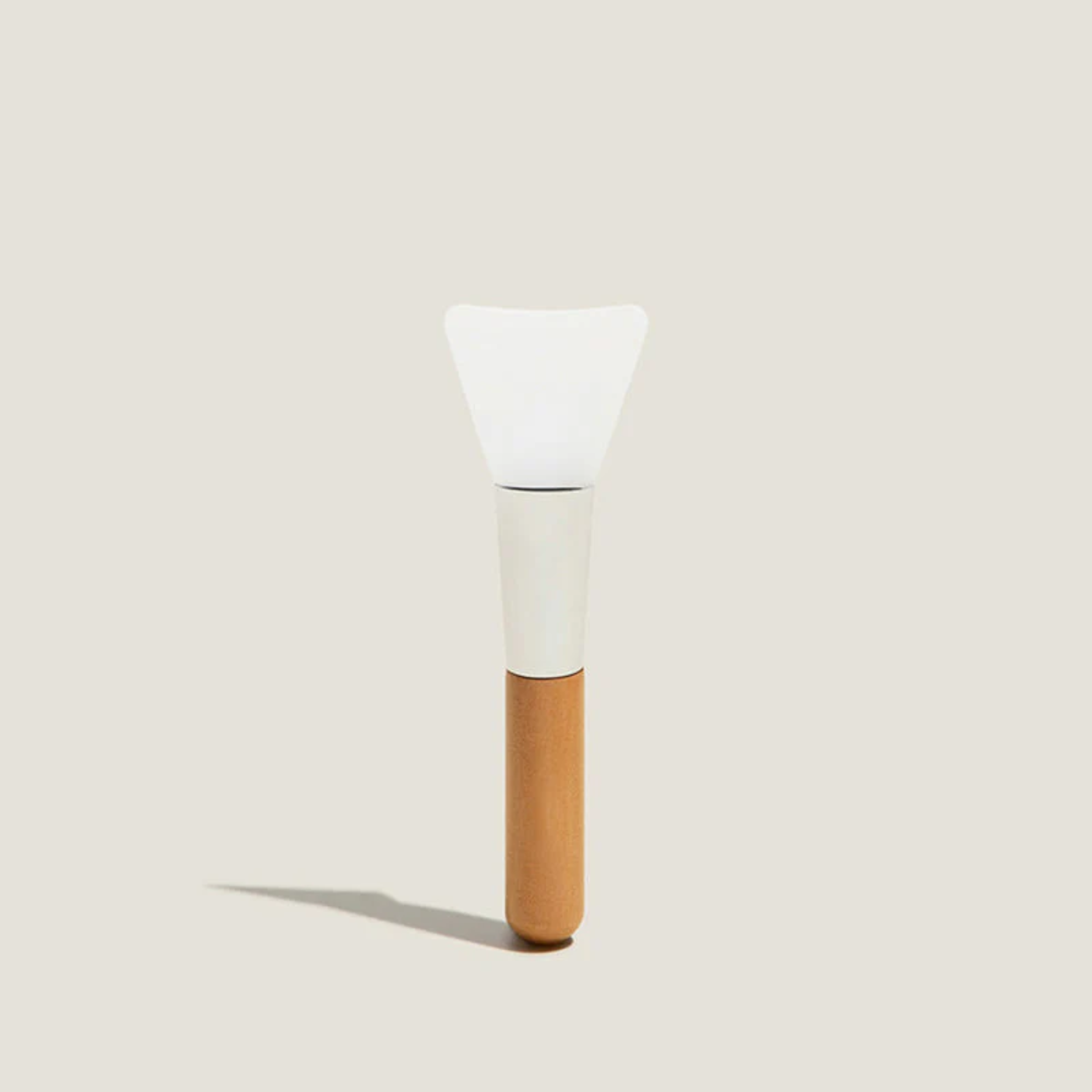 Cosmetic applicator with a white head and brown handle on a light beige background