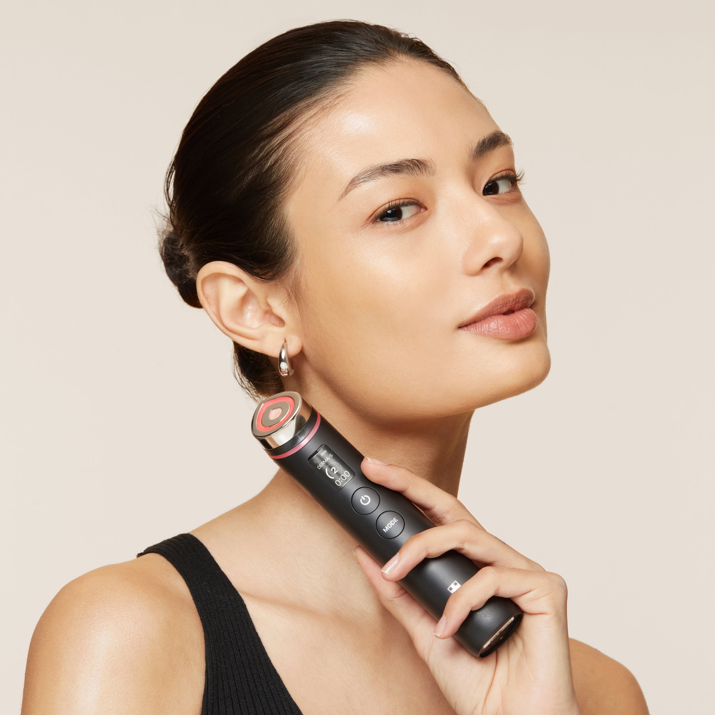 Woman holding a black electronic device against a beige background