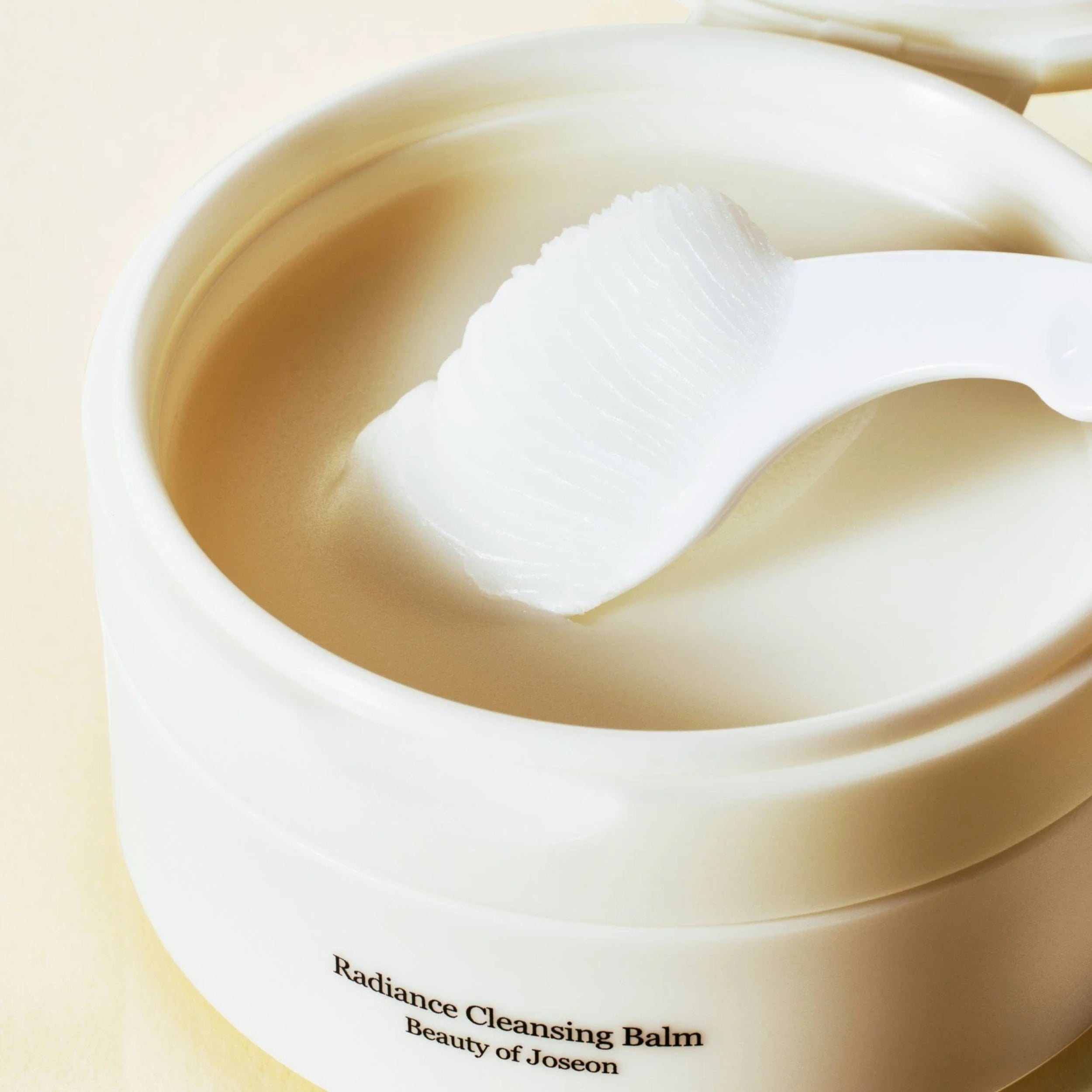Radiance Cleansing Balm container with a white applicator on a beige background