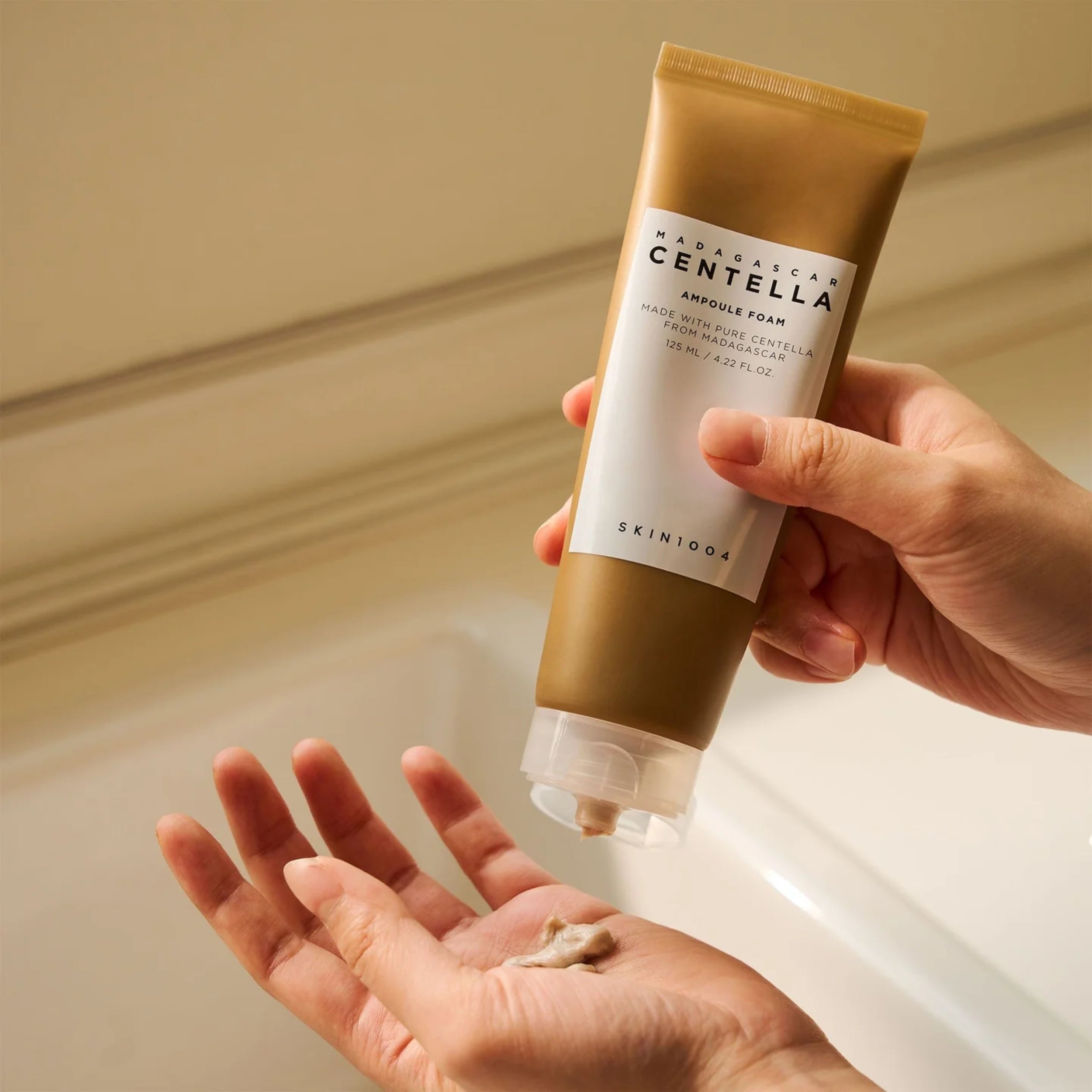 Hand holding a tube of Skintoo Madagascan Centella Astringent Foam over a sink.