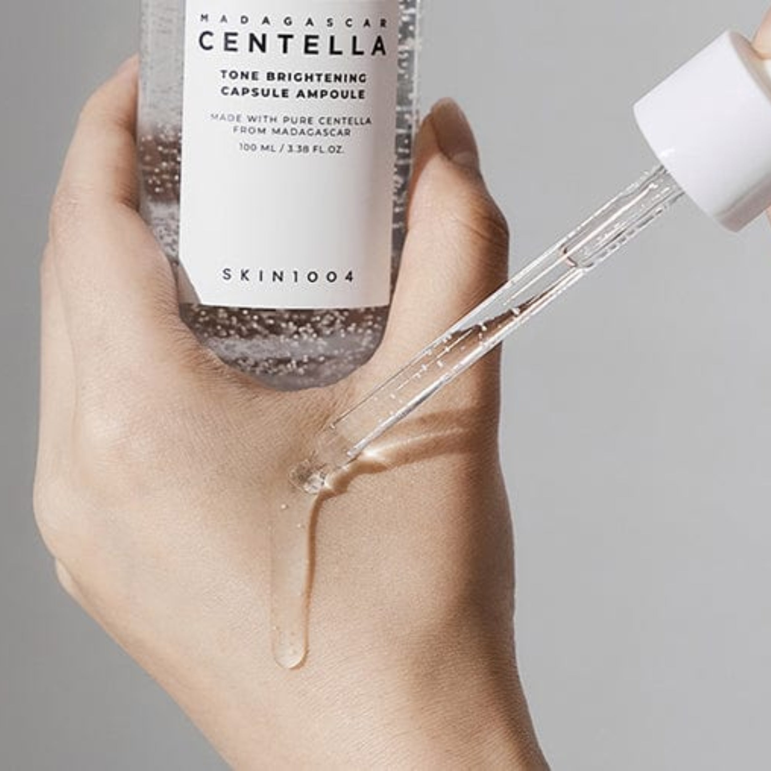 Hand holding a skincare product with a dropper, featuring Skin1004 branding.