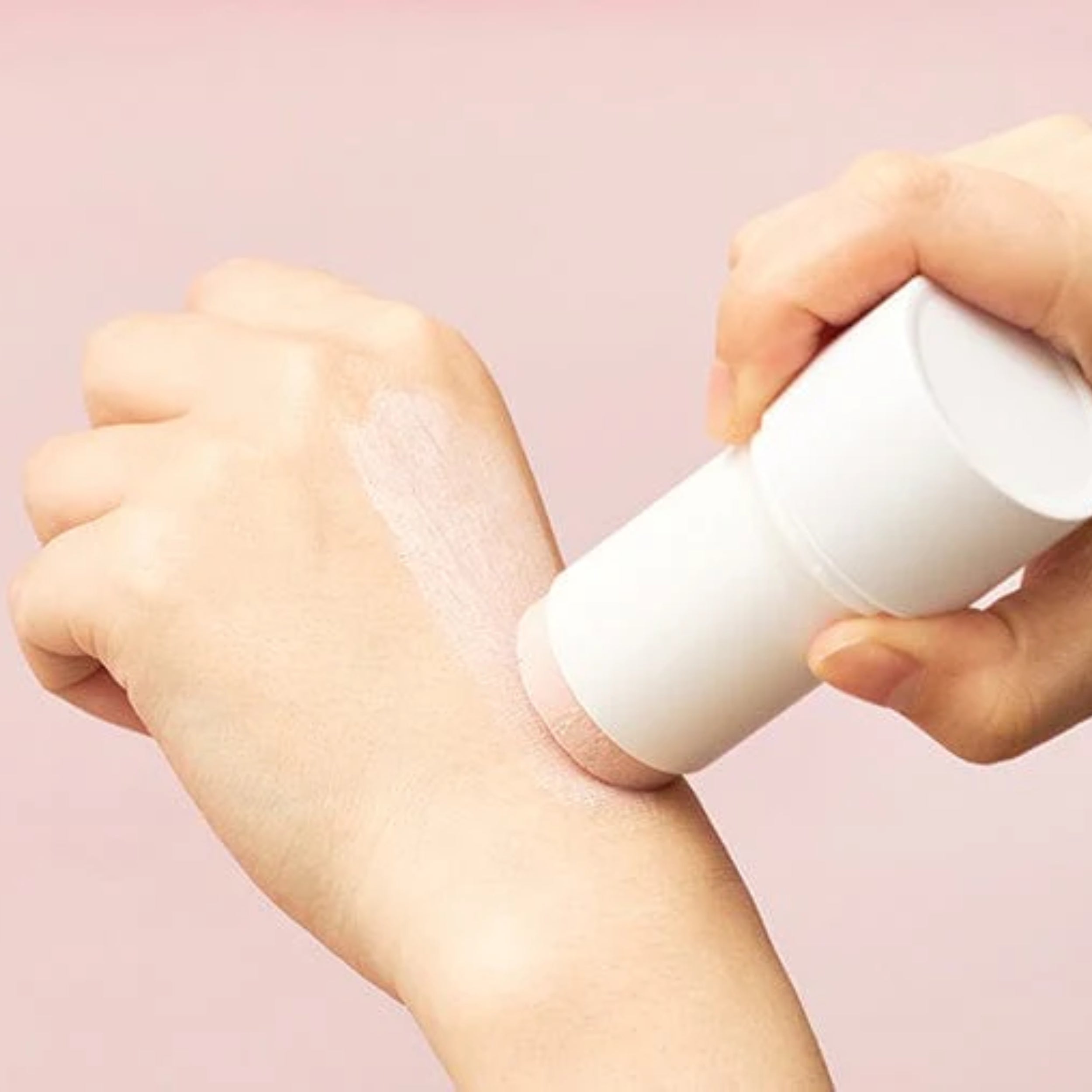 Person applying a white cream or lotion to their wrist against a pink background