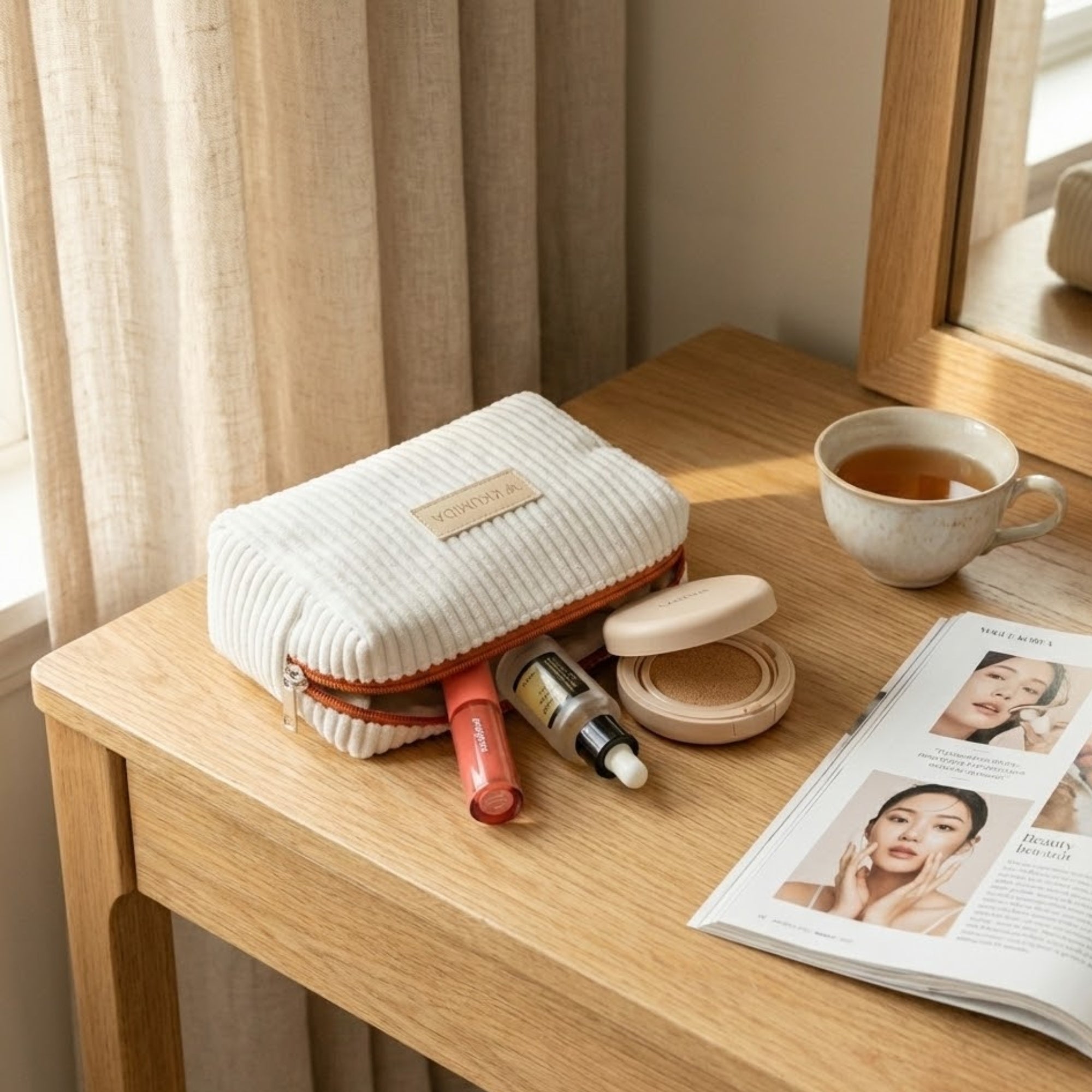 Makeup pouch with cosmetic items on a wooden table next to a cup of tea and a magazine.